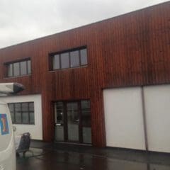 A modern building with a wooden facade, large windows, and a glass door—showcasing expert property refurbishments. The wet ground hints at recent rain, and part of a white van is visible on the left side of the image.