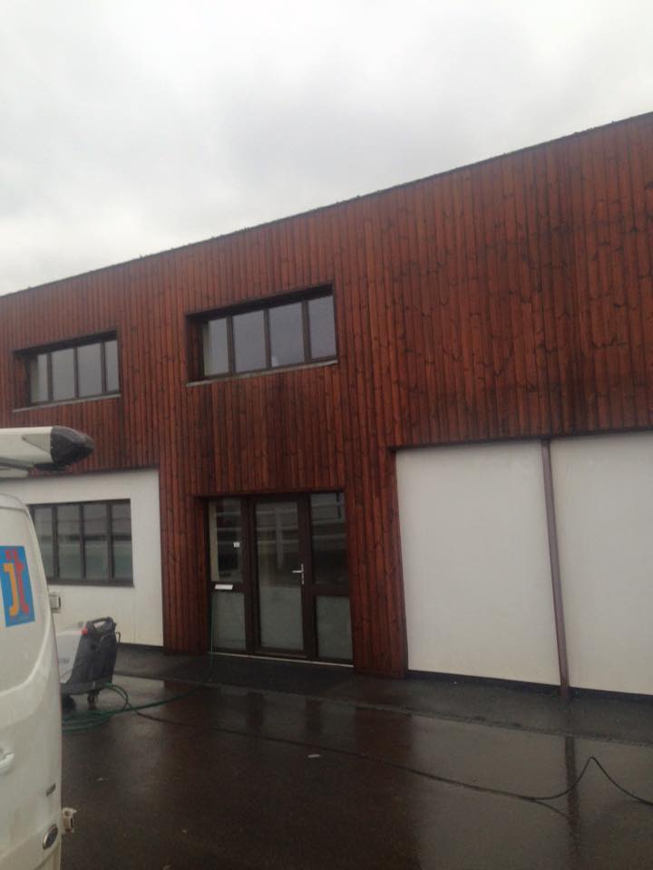 A modern building with a wooden facade, large windows, and a glass door—showcasing expert property refurbishments. The wet ground hints at recent rain, and part of a white van is visible on the left side of the image.