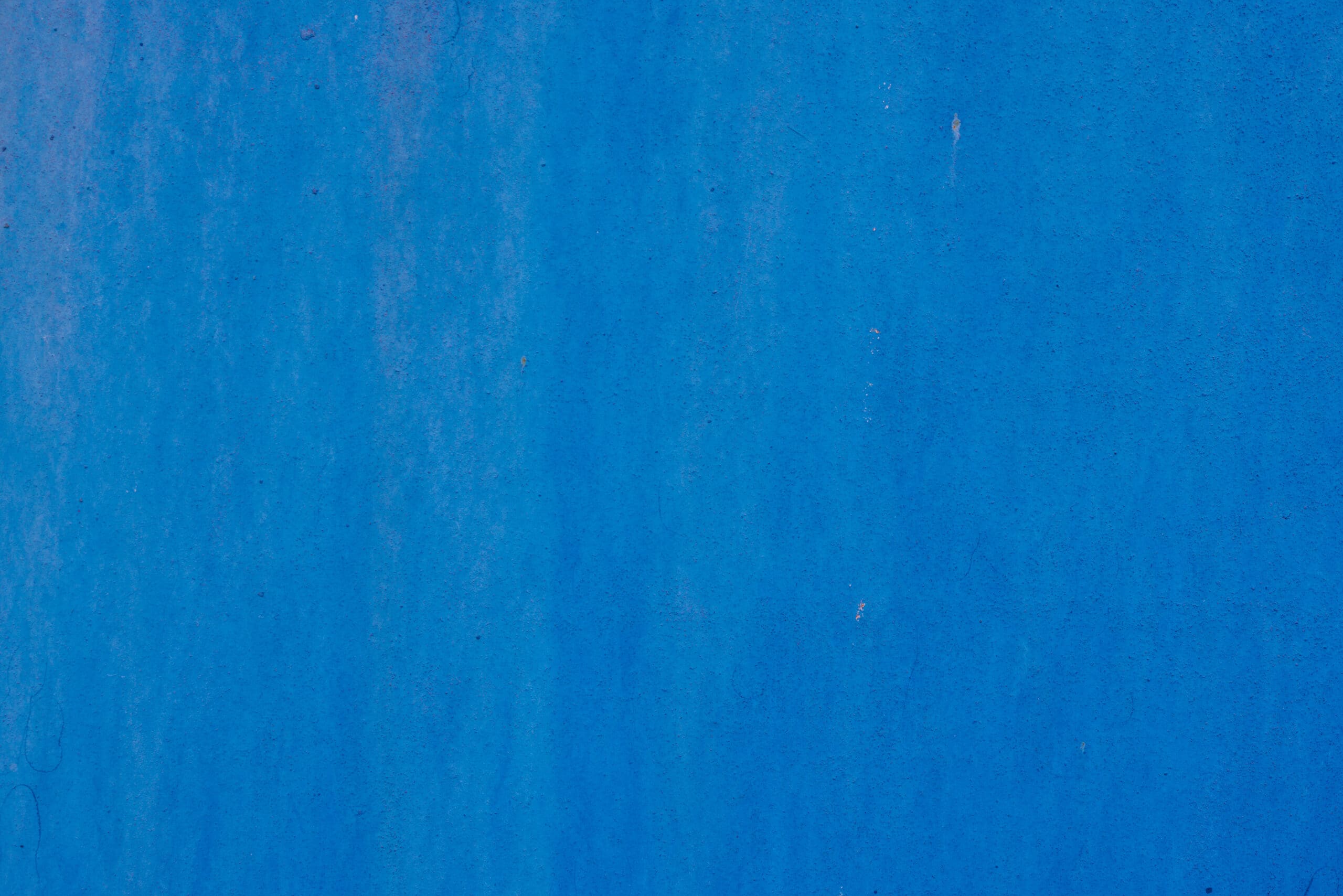 A textured blue wall with subtle variations in shade and faint streaks, perfect for new bathrooms or as part of building maintenance, creating an abstract and slightly weathered appearance.